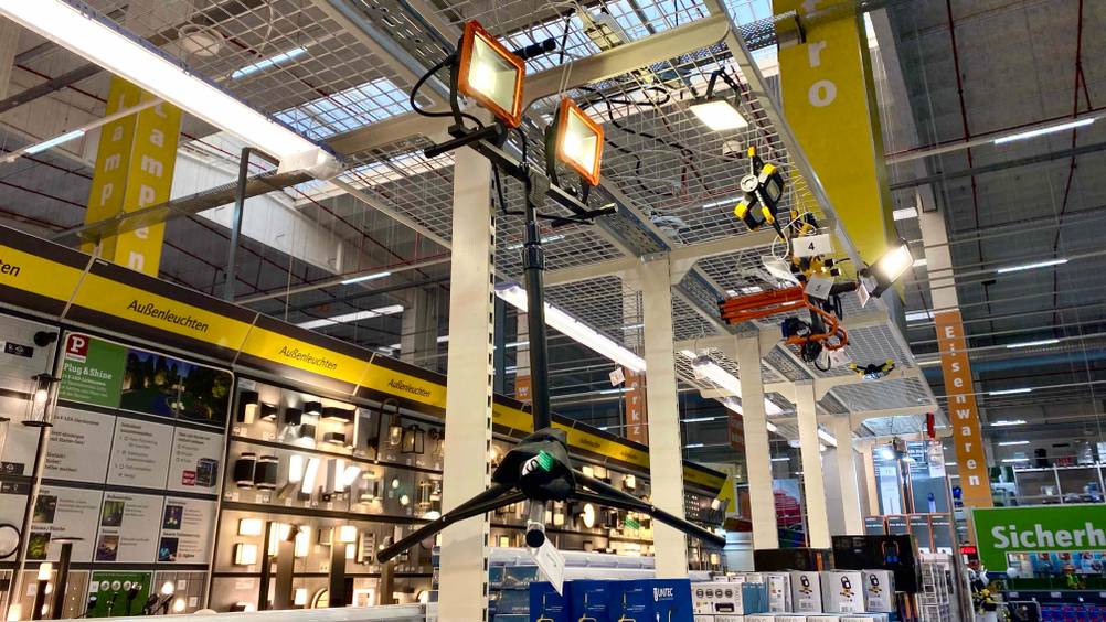Ein getesteter LED-Baustrahler mit Stativ hängt in einer Verkaufsfläche an einem Gitter.