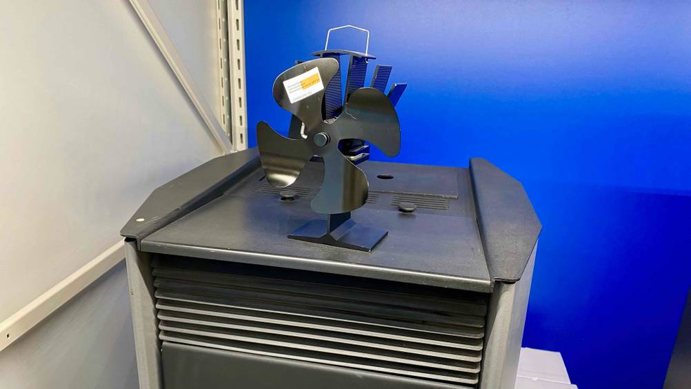 Im Test: Ein Ofenventilator von leicht seitlich auf einem Ofen stehend vor einer blauen Wand.
