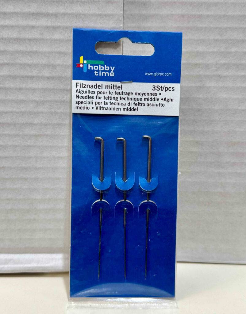 Filznadel-Test: Eine blaue Packpappe mit drei Filznadeln steht vor einem weißen Karton.