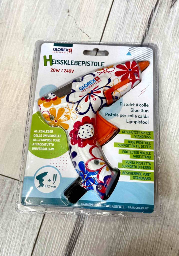 Die getestete 7-mm-Heißklebepistole liegt innerhalb der Verpackung auf einem Holzboden.