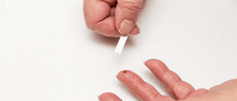 Glukose-Teststreifen im Test: Ein Teststreifen über einem Finger mit Blut.