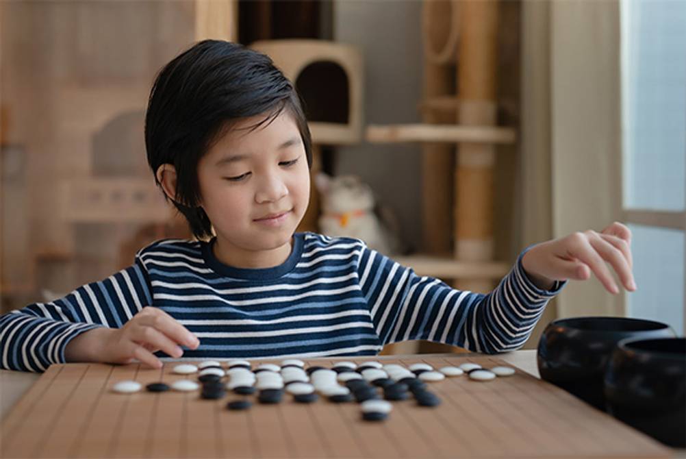 Go-Spiel im Test: Ein Kind welches vor einem Go-Spielbrett sitzt und spielt.