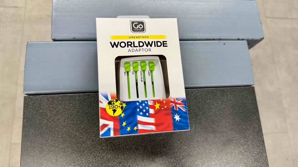Der Weltweit-Reiseadapter liegt innerhalb der Verpackung auf einem schwarz-grauen Hocker.