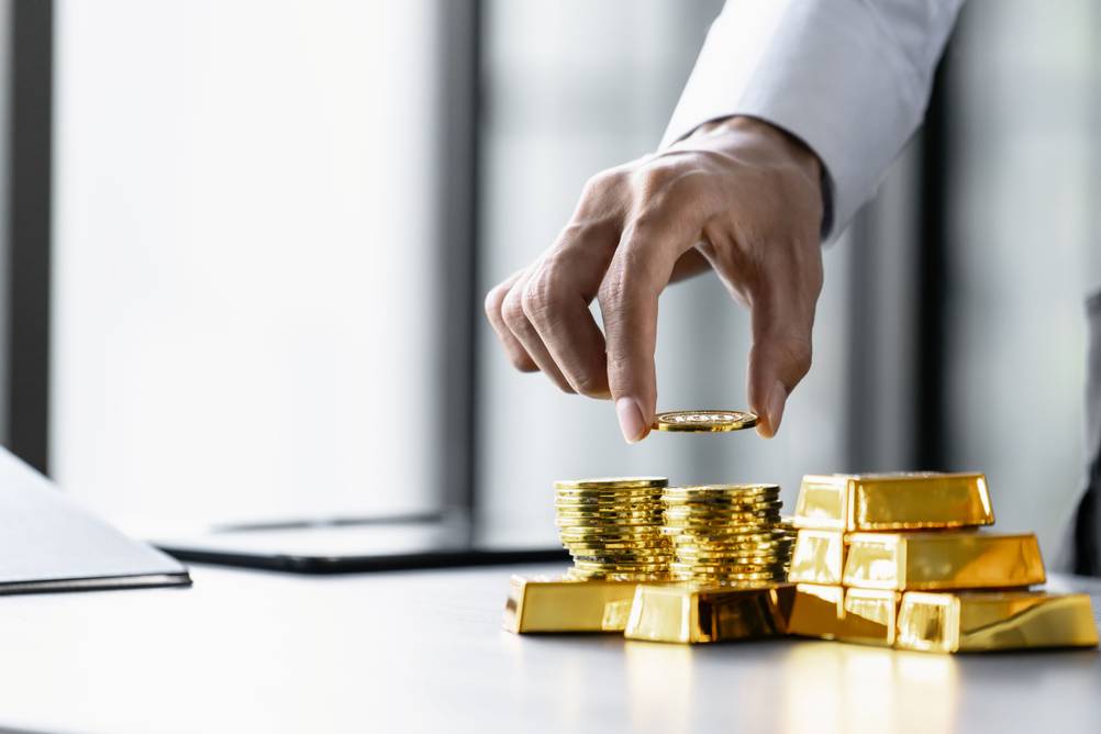 Ein Mann stapelt Goldmünzen und Goldbarren.