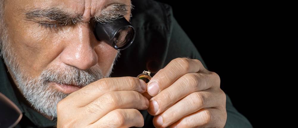 Ein Goldankäufer prüft ein Schmuckstück mit einer Lupe.