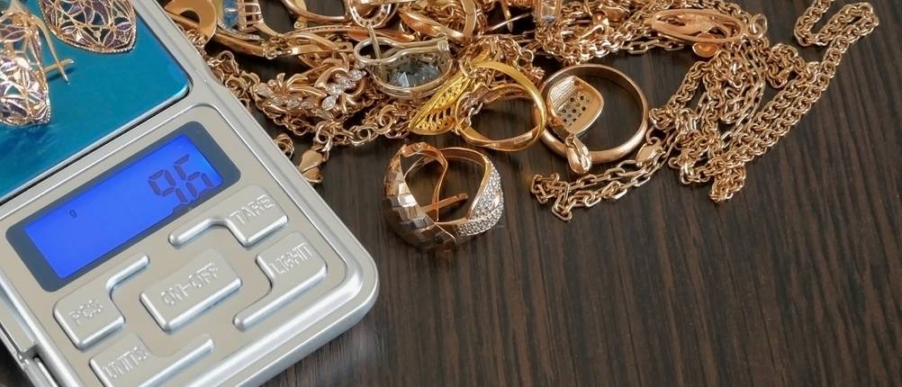 Neben einer Feinwaage liegt eine Menge an unterschiedlichem Schmuck auf dem Tisch.