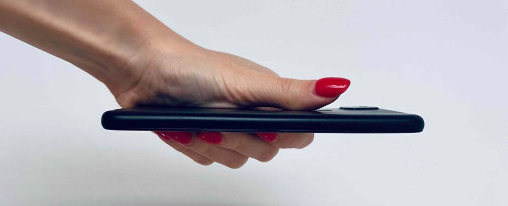 Im Test: ein Google-Pixel in Schwarz, gehalten von einer Damenhand, mit Fokus auf die lange, schmale Seite vor einem weißen Hintergrund.
