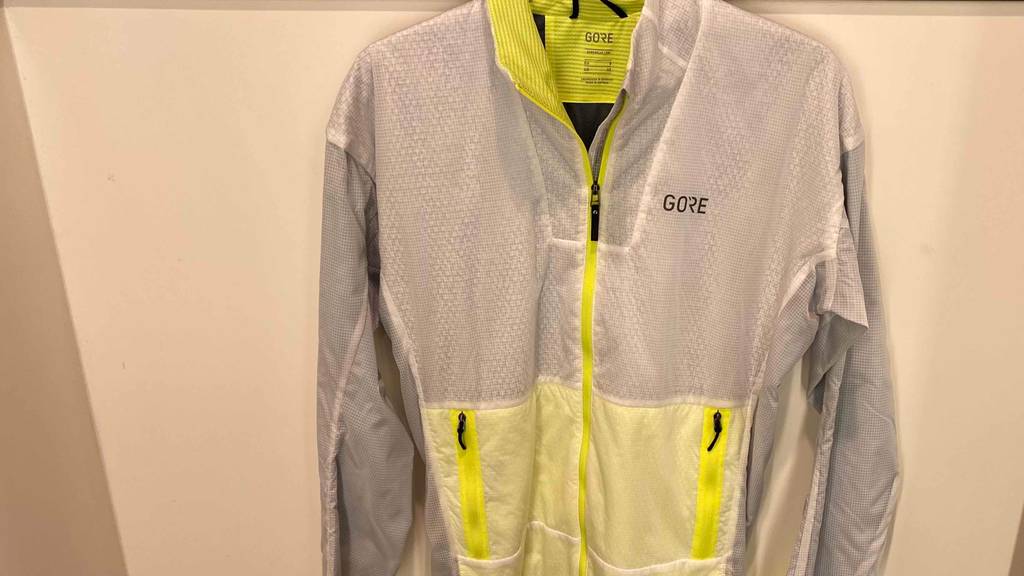 Herren Laufjacke von Gore grau/neongelb, die an einer Wand hängt
