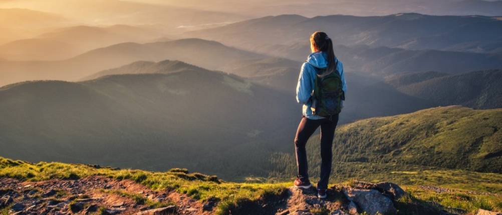 gore-tex-wanderschuhe-damen-test: Eine junge Frau steht auf einem Berg und blickt in die Ferne.