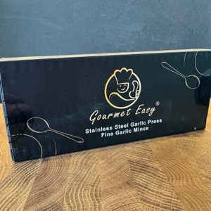 Die Originalverpackung der Gourmet Easy Knoblauchpresse steht auf einem Brett.