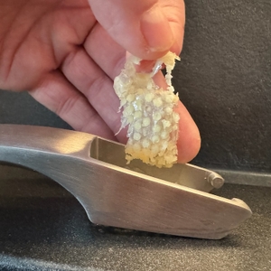 Eine Hand entfernt Knoblauchhaut aus der Knoblauchpresse.