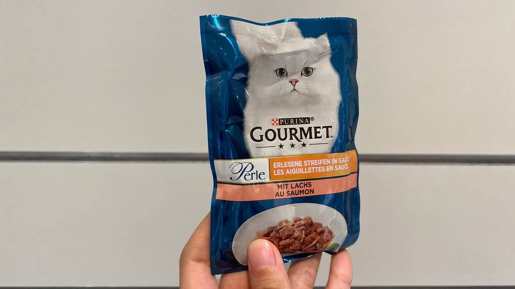 Getestet: Hand hält einen Beutel Gourmet Katzenfutter mit Geschmacksrichtung Lachs vor einem hellen Hintergrund.