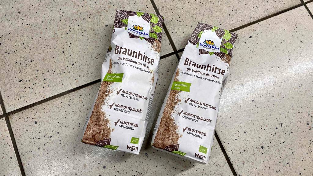 Zwei Verpackungen mit Govinda-Braunhirse im Test liegen auf einem Fliesenboden.