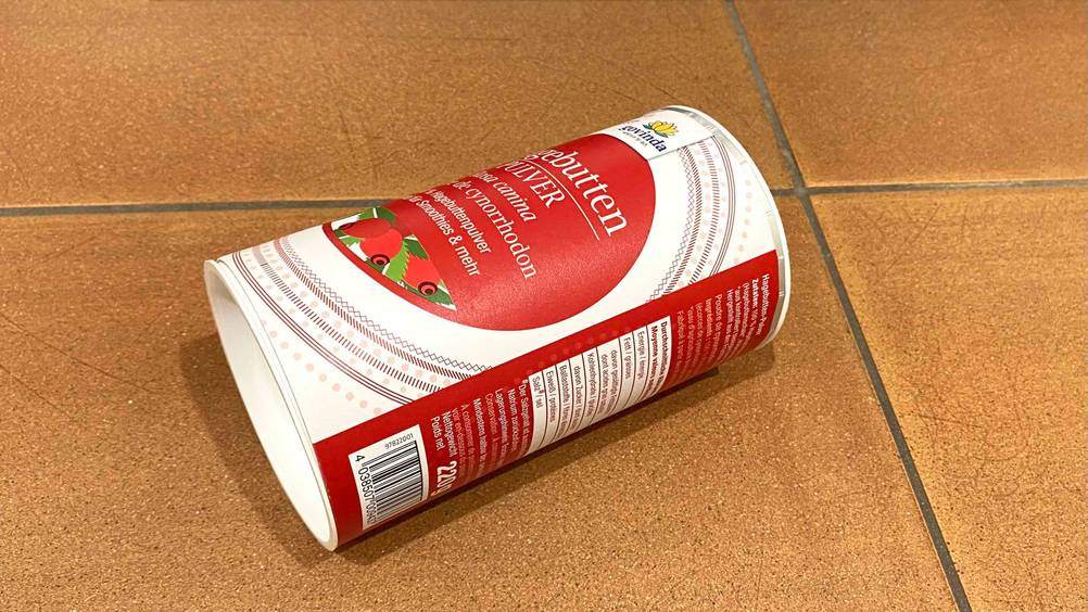 Eine Dose getestetes Hagebuttenpulver liegt mit halb sichtbarer Rückseite auf einem Fliesenboden.