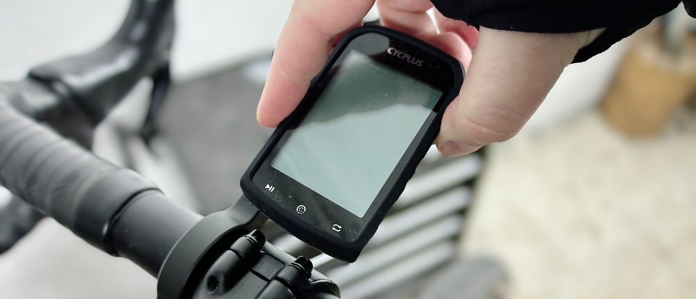 Eine Hand setzt den Cycplus M1 Fahrradcomputer in die Lenkerhalterung ein. Der Lenker eines Rennrads ist im Hintergrund sichtbar.