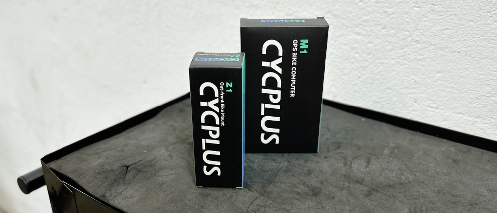 Die Verpackung des Cycplus M1 Fahrradcomputers mit Zubehörbox auf einer dunklen Oberfläche. Das Design ist schlicht und funktional gehalten.