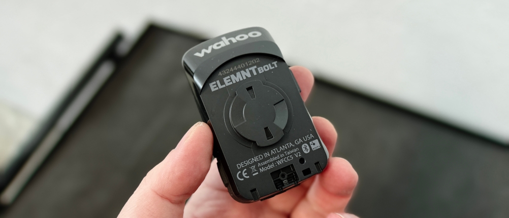 Die Rückseite des Wahoo ELEMNT BOLT V2 Fahrradcomputers mit dem speziellen Befestigungssystem. Eine Hand hält das Gerät vor einem unscharfen Hintergrund.