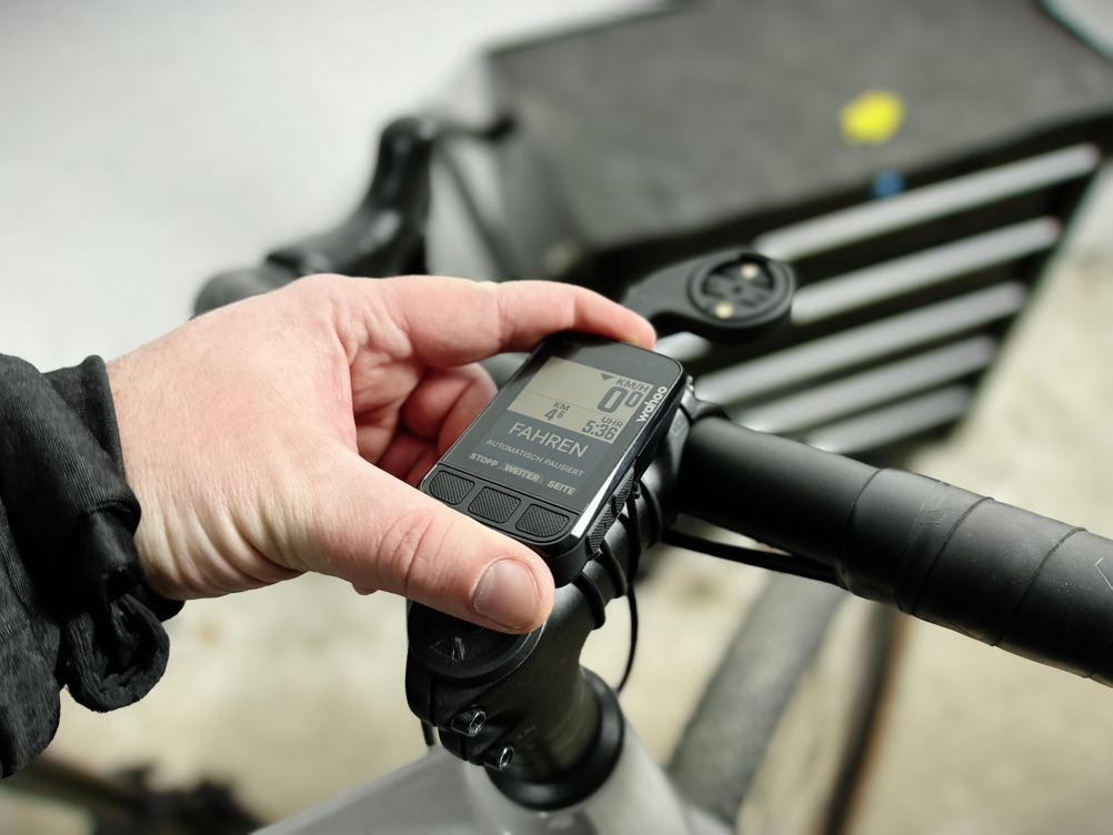Eine Hand befestigt den Wahoo ELEMNT BOLT V2 an einer Fahrradhalterung. Der Fahrradcomputer wird auf eine Lenkerhalterung gedrückt, während der Lenker eines Rennrads zu sehen ist.