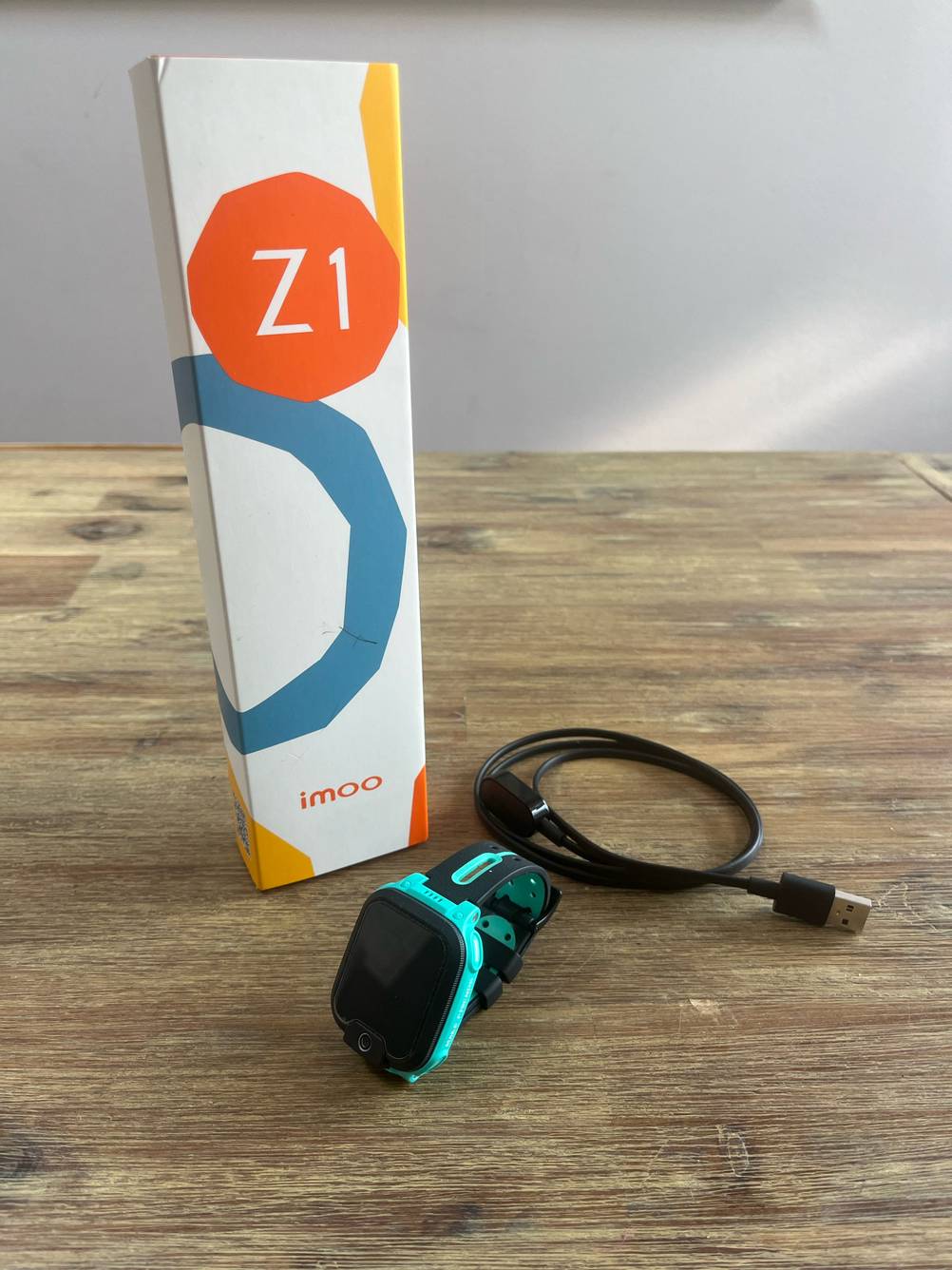 Getestet: Eine GPS-Uhr mit Kabel und Originalverpackung auf einer Holzfläche.