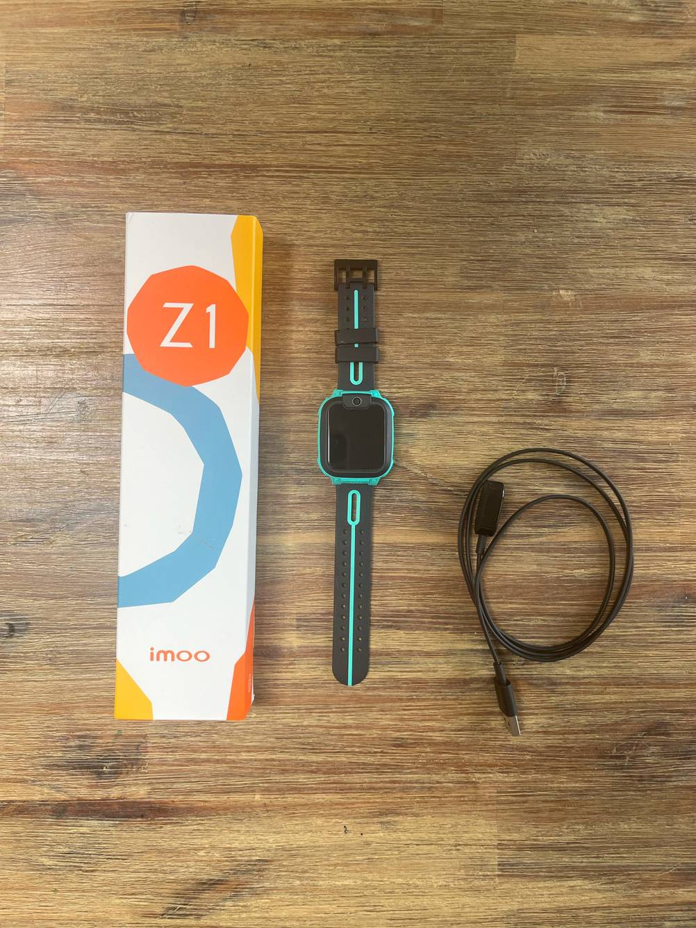 GPS-Uhr getestet: Eine Uhr in der Mitte zwischen Originalverpackung und Ladekabel auf einer Holzfläche.