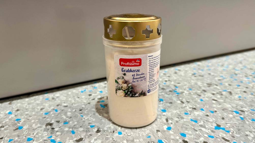 Eine Grabkerze im Test vor einer grauen Wand auf dem Boden.
