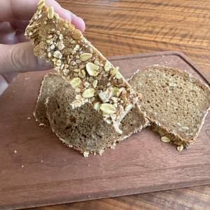 Eine Hand hält eine dick geschnittene Scheibe Vollkornbrot fest