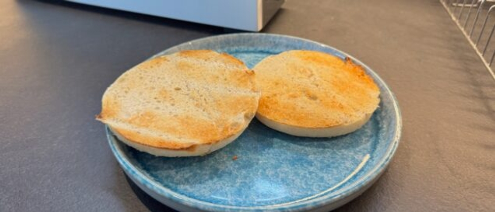 Ein getoastetes, geschnittenes Brötchen liegt auf einem Teller.