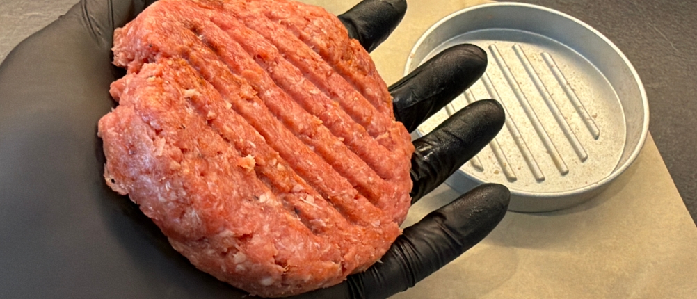 Eine Hand hält ein Burger-Patty aus dem Gräwe-Hamburgerpressen-Set fest