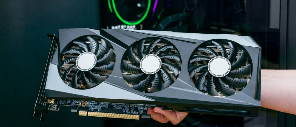 Grafikkarten im Test: Eine Person hält vor einem Computer eine Grafikkarte hoch.