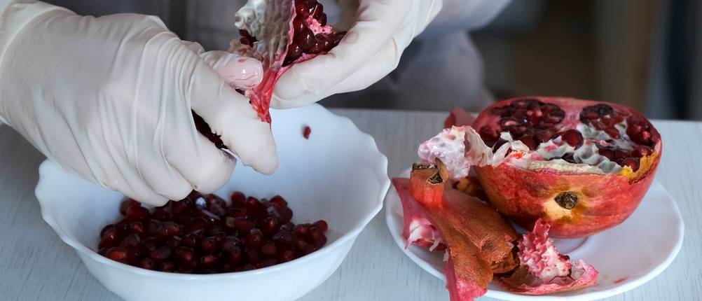 Granatapfel-Entkerner-Test: Eine Frau mit Gummihandschuhen schält einen Granatapfel über einer Schüssel.