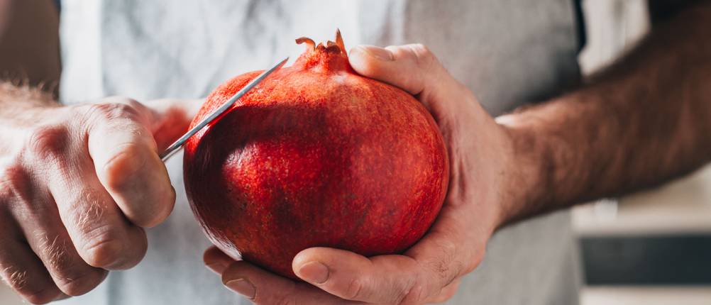 Granatapfel-Entkerner-Test: Mann schneidet einen Granatapfel mit einem Messer.