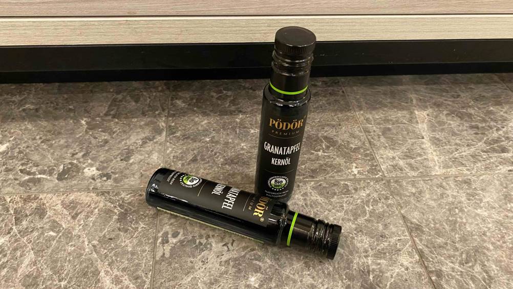 Ein Granatapfelkernöl im Test: Zwei Glasflaschen gefüllt mit Granatapfelkernöl befinden sich auf dem Boden.