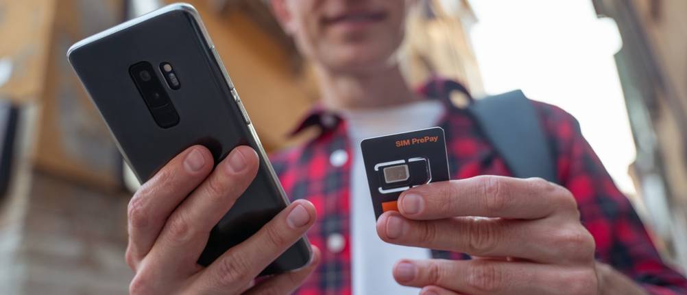 Ein Mann hält eine Prepaid-SIM-Karte und sein Smartphone in den Händen.