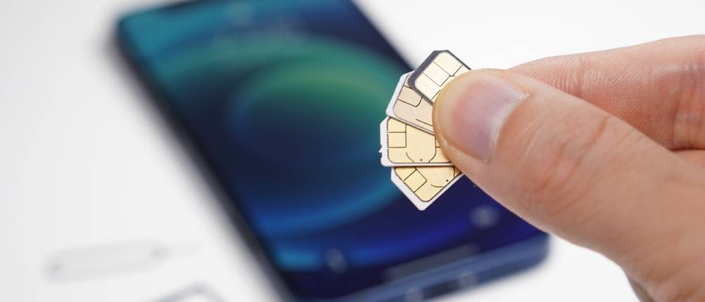Zwei Finger halten mehrere SIM-Karten vor einem Smartphone in die Höhe.