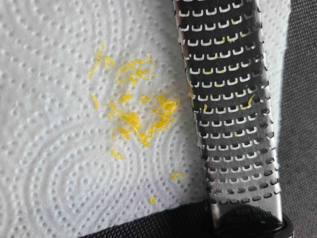 Neben der getesteten Microplane-Reibe liegt geriebene Zitronenschale auf einem weißen Papiertuch.