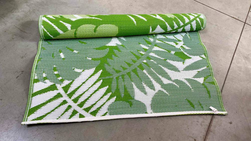 Outdoor-Teppich-Test: Ein halb ausgerollter grün-weißer Teppich liegt auf einem grauen Boden.
