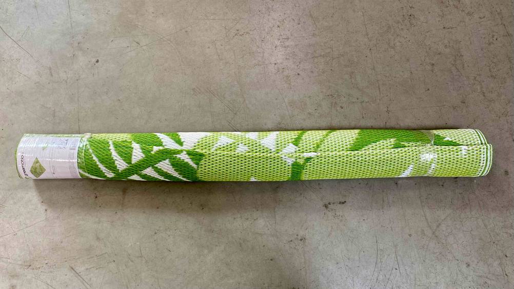 Ein eingepackter grün-weißer Outdoor-Teppich im Test horizontal auf einem Betonboden.