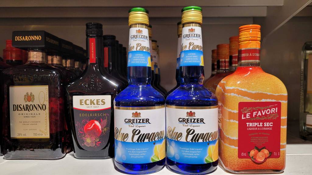 Eine Flasche mit getestetem Blue-Curacao-Sirup steht neben Spirituosen in einem Getränkeregal im Supermarkt.