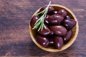 Griechische Oliven im Test: In einem kleinen Holzschälchen befinden sich Kalamata-Oliven und etwas Rosmarin. 