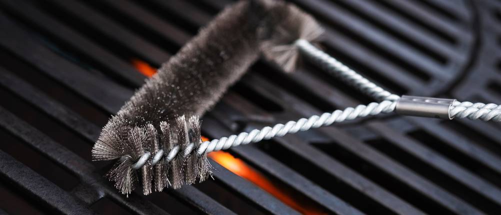 Metallbürste reinigt Grillrost vor der nächsten Nutzung.