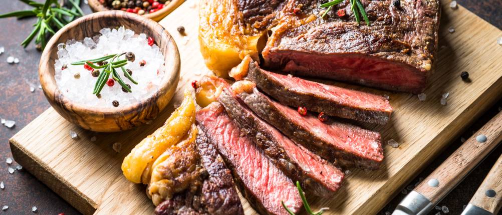 Grillen mit einem Oberhitzegrill: Aufgeschnittenes Steak liegt auf einem Holzbrett neben einer Salzschüssel.