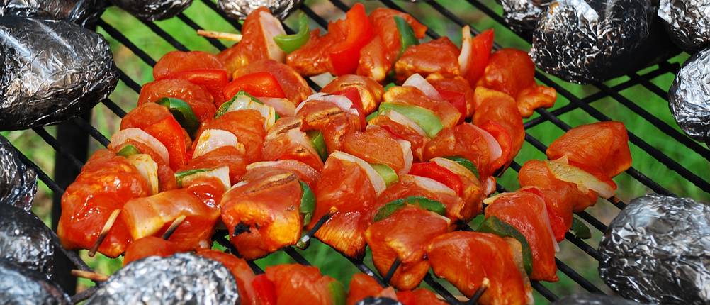 Auf einem Schwenkgrill werden Gemüsespieße und Folienkartoffeln gegart.