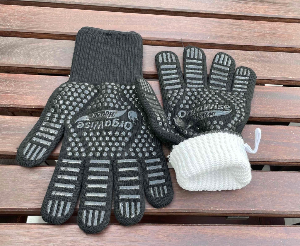 Schwarze Grillhandschuhe im Test: Sie liegen mit der gummierten Innenseite nach oben und das weiße Innengewebe ist sichtbar.