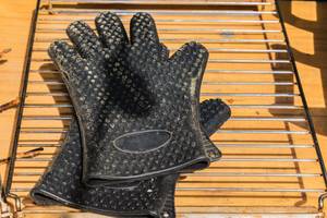 Grillhandschuhe im Test: Grillhandschuhe mit Noppen liegen auf einem Rost.