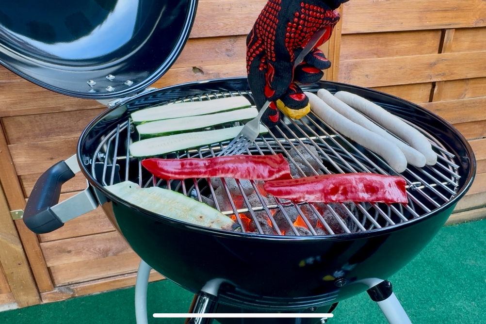 Eine Person dreht mit einer Gabel und den getesteten Grillhandschuhen von Primajor etwas auf dem Grillrost um.