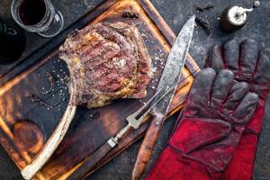 Grillhandschuhe im Test: Grillhandschuhe neben Steak auf einem Schneidebrett.