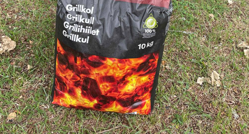 Nahaufnahme der Verpackung der getesteten Grillkohle mit kg-Angaben auf einer Wiese.