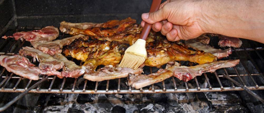 Fleisch auf einem Grillrost wird mit Silikonpinsel bestrichen.