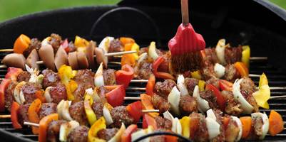 Fleischspieße auf einem Grill werden mit einem Grillpinsel bestrichen.