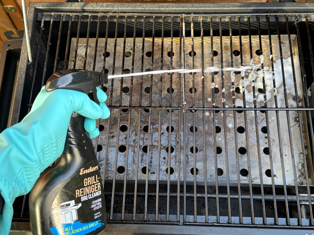 Eine Person sprüht im Test mit dem Enders-Grillreiniger einen Grillrost ein.